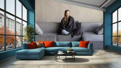 cutewoman relaxing o the sofa wrapped in a soft grey blanket Wall mural